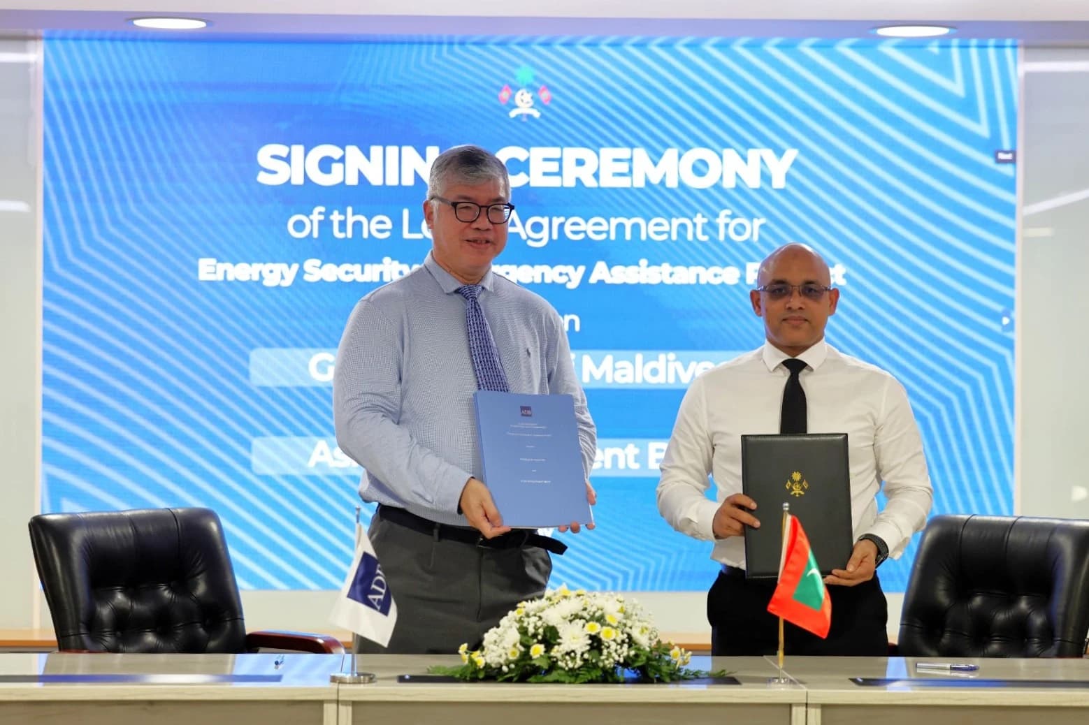 Finance Minister Hassan Zareer and ADB’s Thiam Hee Ng hold signed agreement folders at a signing ceremony, with Maldivian and ADB flags on the table.