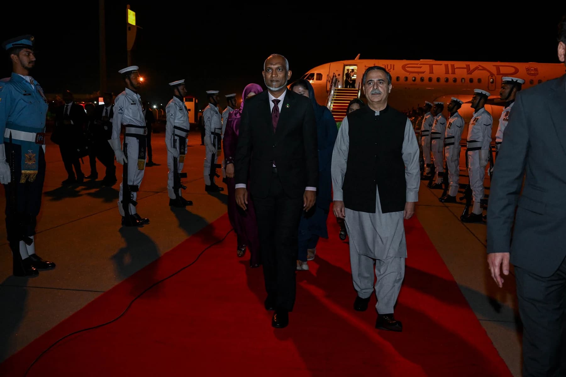 President Mohamed Muizzu walks along a red carpet past a guard of honour at night, beside a Pakistani official.