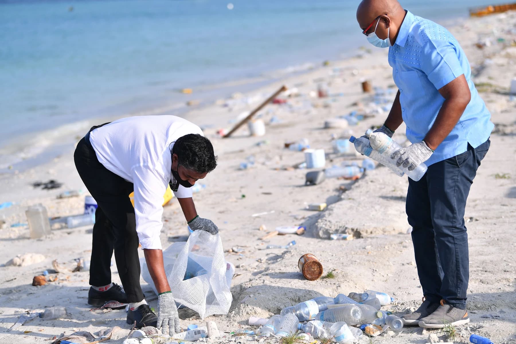 Two volunteers collecting discarded plastic bottles on a beach in Hulhumalé