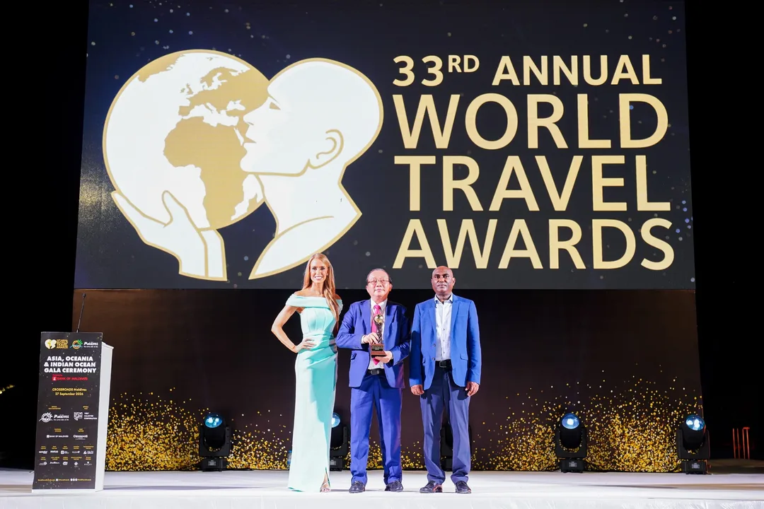 A Vietjet representative holds a World Travel Awards trophy on stage beside two other people, in front of a large World Travel Awards screen.
