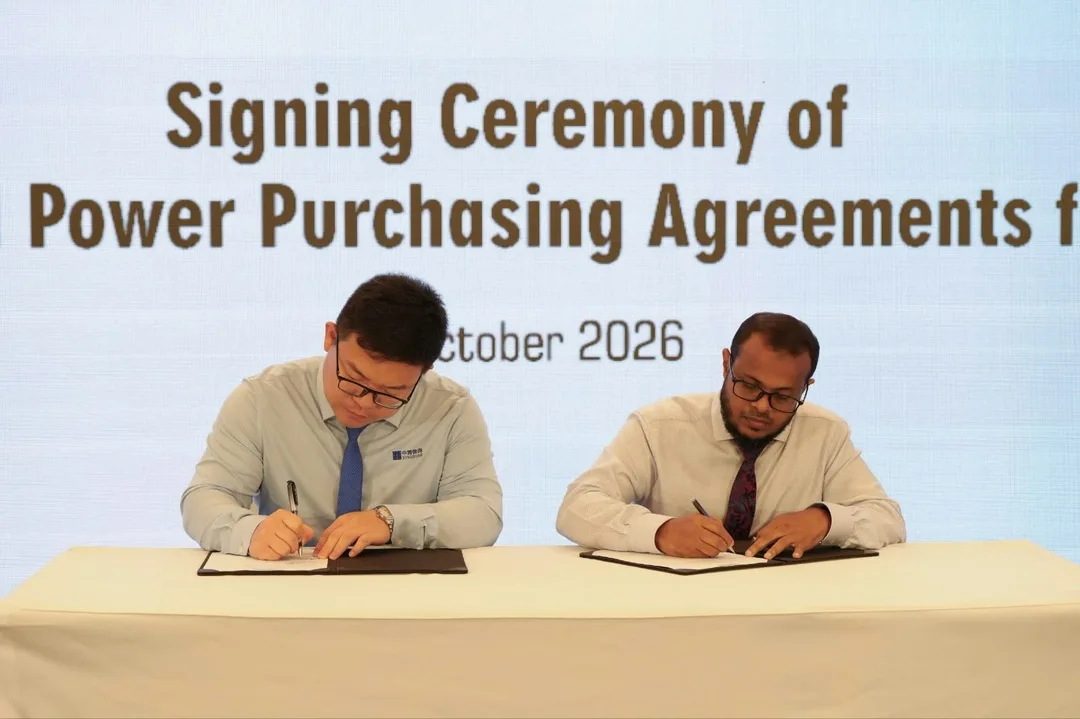 Two men in shirts and ties sign documents at a table draped in white, in front of a screen reading "Signing Ceremony of … Power Purchasing Agreements … October 2026".